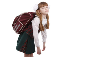 School girl is tired. Schoolgirl in school uniform with backpack. Pupil's satchel is very heavy.  Sad teenager. A heavy load to bear. Isolated on white in studio.